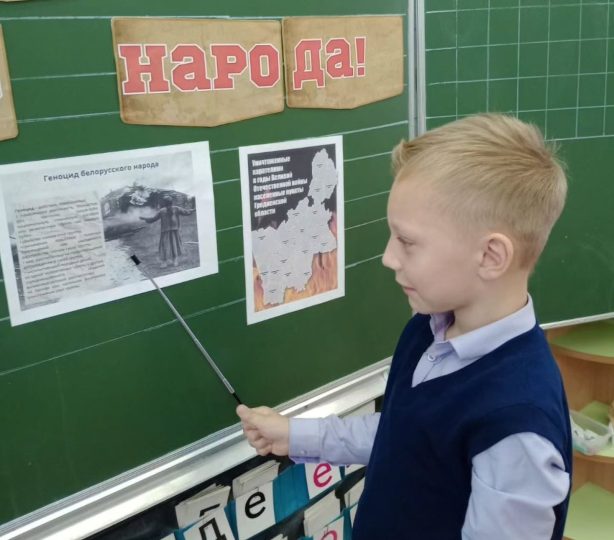 Школьник стоит у доски и указывает указкой на геноцид беларуского народа