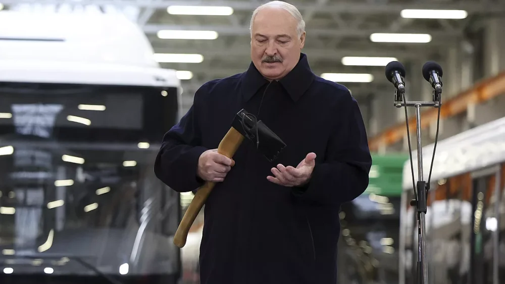 Александр Лукашенко держит топор во время визита на промышленное предприятие. На фоне — производственный цех и автобусы.