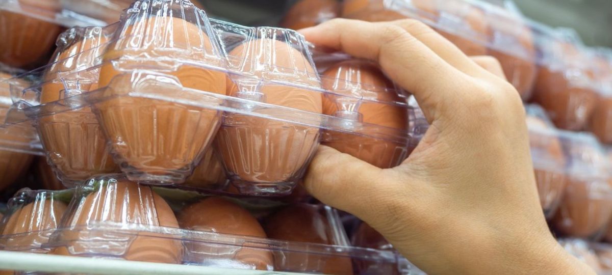 Человек берет яйца с полки в магазине